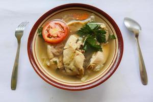 Chicken soup served with vegetables, tomatoes, celery in a bowl, spoon and fork. with black background photo
