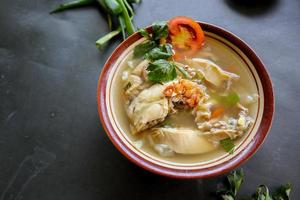 Chicken soup served with vegetables, tomatoes, celery in a bowl, spoon and fork. with black background photo