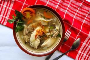 Chicken soup served with vegetables, tomatoes, celery in a bowl, spoon and fork. with black background photo