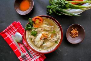 Chicken soup served with vegetables, tomatoes, celery in a bowl, spoon and fork. with black background photo