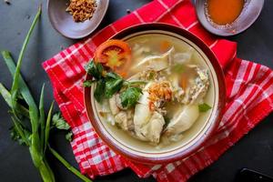 Chicken soup served with vegetables, tomatoes, celery in a bowl, spoon and fork. with black background photo