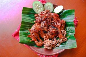 grilled chicken or ayam bakar with cucumber slash served on banana leaf and plate. ayam bakar is traditional grilled chicken from indonesia photo