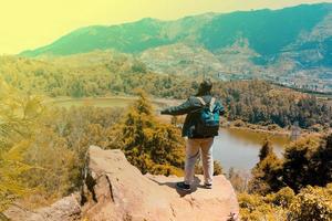 man standing on a rock of a cliff and enjoying the view of nature of lake and mountain. symbol of freedom photo