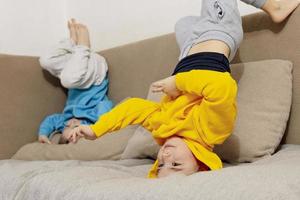 Two little caucasian kids doing gymnastic handstand exercise in living room. Children standing on hands upside down and having fun together. Sport at home. Workout in the apartment. Healthy lifestyle. photo