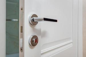 Modern metal door handle on white wooden door in interior. Knob close-up elements. Door handle, fittings for interior design photo