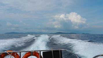 vista da parte de trás de uma lancha. ondas dos motores de um barco de alta velocidade. céu azul, nuvem branca e ilha distante. espuma branca das ondas. flutuando no oceano. video