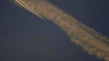 4K Beautiful plane trail at sunset yellow light on blue sky, aircraft layer pollution video