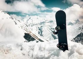 Snowboard stand in snow with beautiful white caucasus mountains background in Gudauri ski resort top viewpoint in winter. Georgia skiing winter holiday destination photo