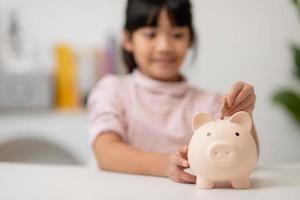 Little Asian girl saving money in a piggy bank, learning about saving, Kid save money for future education. Money, finances, insurance, and people concept photo