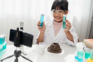 Asian school girl making easy chemistry experiments and recording a video for his followers, Young blogger kid posing in front of camera for vlog, Children make vlog for social media channel concept. photo