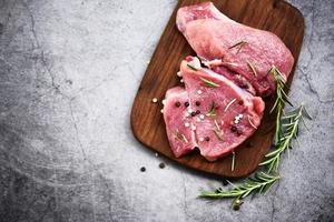 Raw pork meat on wooden cutting board at kitchen table for cooking pork steak roasted or grilled with ingredients herb and spices Fresh pork photo