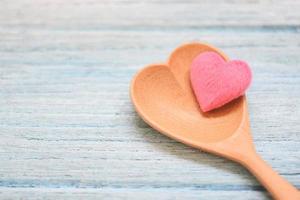 corazón rosa en una cuchara de madera y en el fondo de la mesa de madera, vista superior en forma de corazón de cuchara de café, amor por la salud o amor por la cocina foto