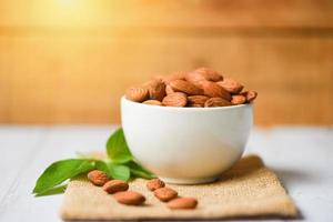 Almonds nuts on bowl with leaf almonds on wooden background - Roasted almond for snack photo