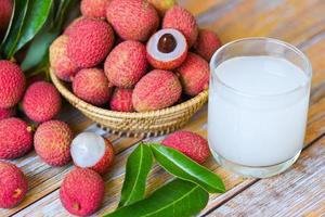 Fresh lychee drink and slice peeled with green leaves harvest in basket from tree tropical fruit summer in Thailand - Lychee juice on wooden table photo