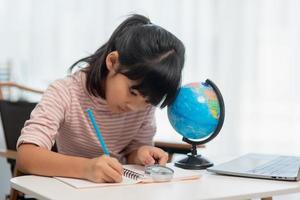 Asian little girl is learning the globe model, concept of save the world and learn through play activity for kid education at home. photo