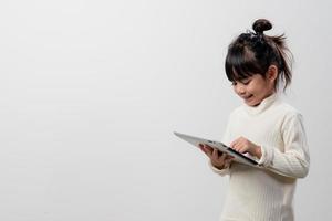 Asian little girl holding and using the digital tablet on white studio background, free copy space photo