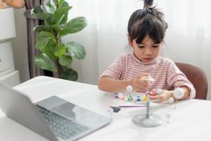 Asian Little girl studies the solar system in geography class. looking at the scale model of planets photo