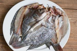 dried fish on white plate, tilapia fish for cooking food on wooden - food preservation dry fish photo