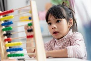 A young cute Asian girl is using the abacus with colored beads to learn how to count at home photo