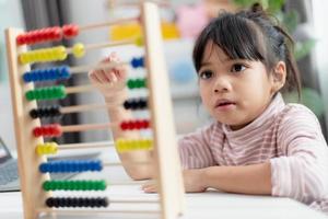 A young cute Asian girl is using the abacus with colored beads to learn how to count at home photo