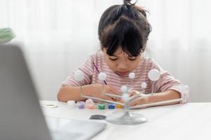 Asian Little girl studies the solar system in geography class. looking at the scale model of planets photo