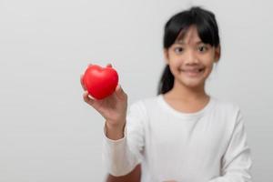 Portrait of Asian little girl child holding red heart sign on white background photo