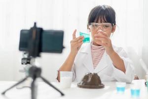 Asian school girl making easy chemistry experiments and recording a video for his followers, Young blogger kid posing in front of camera for vlog, Children make vlog for social media channel concept. photo