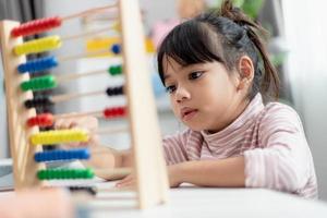 A young cute Asian girl is using the abacus with colored beads to learn how to count at home photo