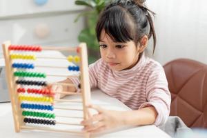 una joven asiática linda está usando el ábaco con cuentas de colores para aprender a contar en casa foto