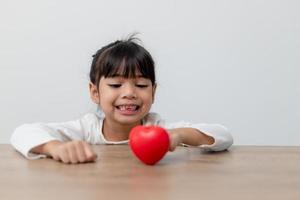 Portrait of Asian little girl child holding red heart sign on white background photo