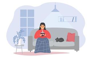 The girl is sitting on the sofa with a cup of hot drink under the blanket. A woman is warming herself under a blanket with a pet cat next to her. Vector graphics.