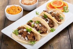 Pork carnitas tacos with onion and cilantro served with rice and refried beans photo