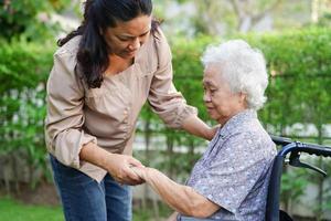 Caregiver help Asian elderly woman disability patient sitting on wheelchair in park, medical concept. photo