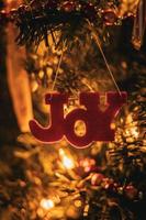 adorno navideño de alegría colgando de un árbol de navidad con luces suaves foto