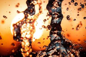 stream of water with droplets and bubbles under the orange and yellow rays of the sun. Texture of water waves of a large fountain photo