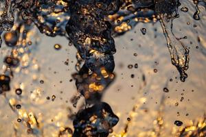 chorros de agua con muchas gotas y burbujas bajo el sol sobre un fondo amarillo anaranjado. un gran plan la textura de las ondas de agua de una gran fuente foto