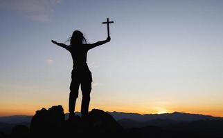 silueta de una joven cristiana rezando con una cruz al amanecer, fondo del concepto de religión cristiana. foto