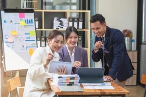 Asian business team consists of marketing staff. accountant and financial officer Help each other analyze company profits using tablets. calculator Laptop computers, graph paper, and corporate pens. photo