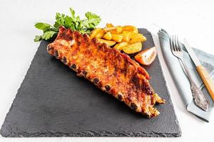 pork ribs are served on an slate board with slices of grilled potatoes and parsley greens. space for your text on a piece of slate board. menu. photo