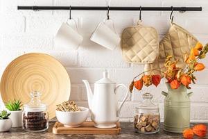cafetera de porcelana blanca, latas de azúcar y granos de café, galletas de frijoles en un bol. fondo moderno de cocina. foto