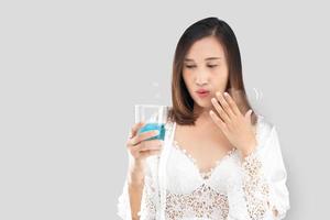 Asian woman in a satin white nightgown wearing a lace robe feels a burn in her mouth because of using mouthwash. Female using gargle in the morning. Add gray space on the left side. photo