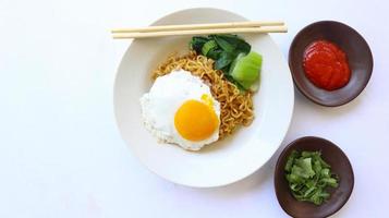 instant noodles served with egg fried and mustard greens on plate. instant fried noodle indomie photo