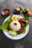 nasi lemak, es un malayo tradicional hecho con huevos cocidos, frijoles, anchoas, salsa de chile, pepino. del plato servido en una hoja de plátano foto