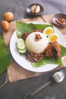 nasi lemak, is traditional malay made boiled eggs, beans, anchovies, chili sauce, cucumber. from dish served on a banana leaf photo