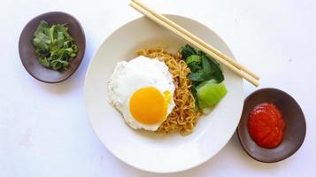 fideos instantáneos servidos con huevo frito y hojas de mostaza en un plato. indomie de fideos fritos instantáneos foto