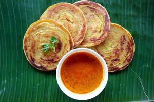 pan paratha o pan canai o roti maryam, plato de desayuno favorito. servido en licencia de plátano foto