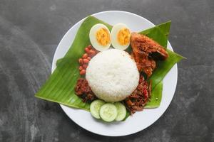 nasi lemak, es un malayo tradicional hecho con huevos cocidos, frijoles, anchoas, salsa de chile, pepino. del plato servido en una hoja de plátano foto