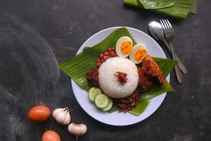 nasi lemak, es un malayo tradicional hecho con huevos cocidos, frijoles, anchoas, salsa de chile, pepino. del plato servido en una hoja de plátano foto