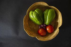 tomates tropicales con jipang o labu siam o chayote y cebolla se sirven en una cesta aislada de fondo negro foto