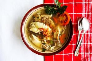 Chicken soup served with vegetables, tomatoes, celery in a bowl, spoon and fork. with black background photo